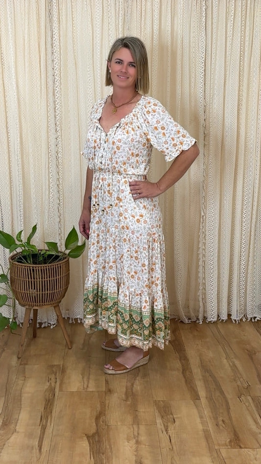 Woman wearing Amber Bloom Maxi Dress by Solara Boheme with floral print and green border standing indoors near plant