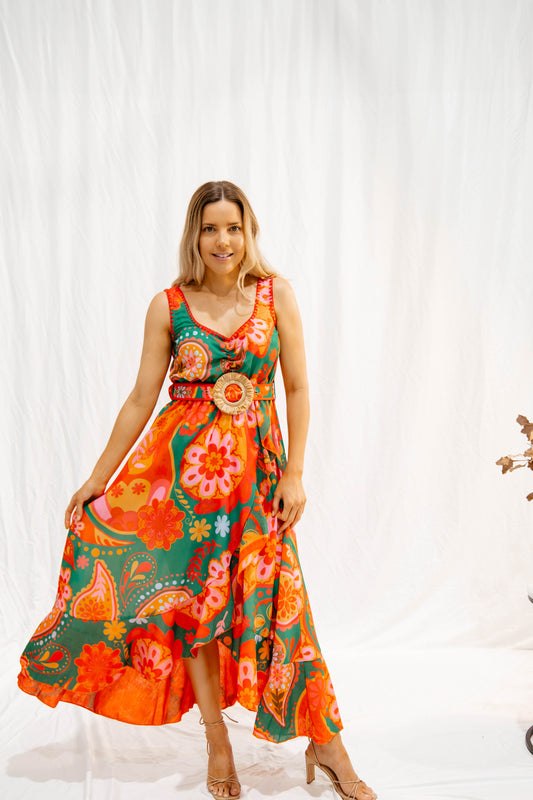 Woman wearing colorful maxi dress with rattan belt standing against white backdrop