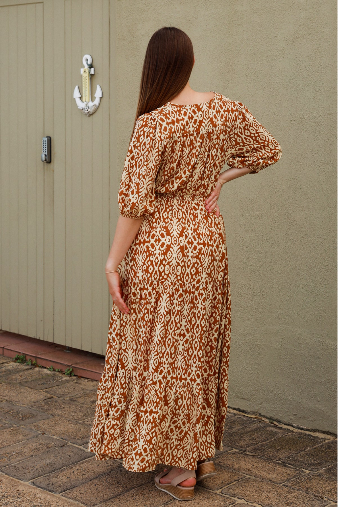 Woman wearing the Cora Maxi Dress by Solara Boheme with an exclusive brown and cream print, standing outdoors.