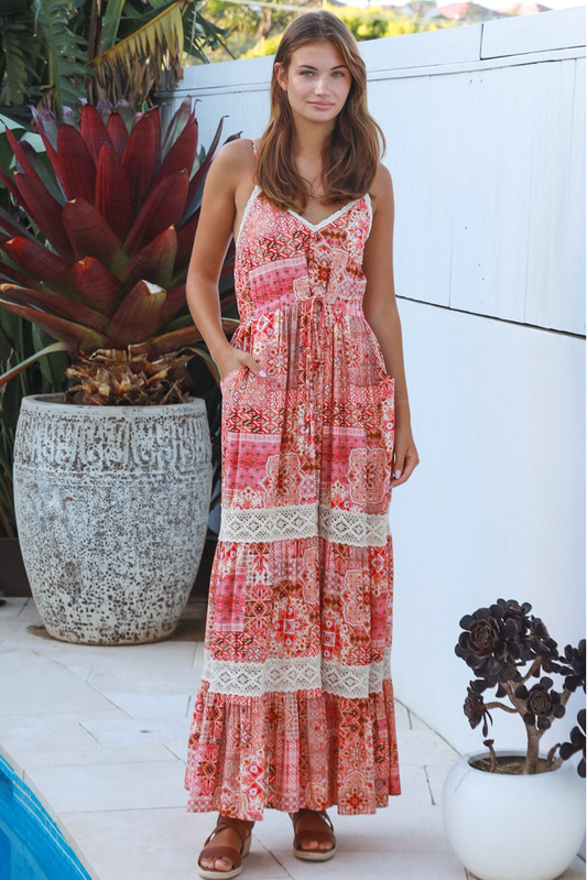 Woman in a red and white patterned dress standing outdoors with plants around.