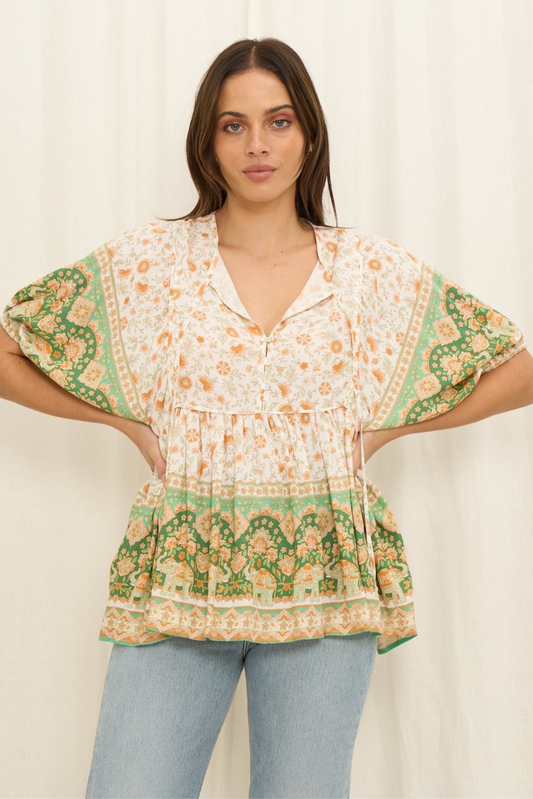 Woman wearing a patterned blouse with balloon sleeves against a plain background