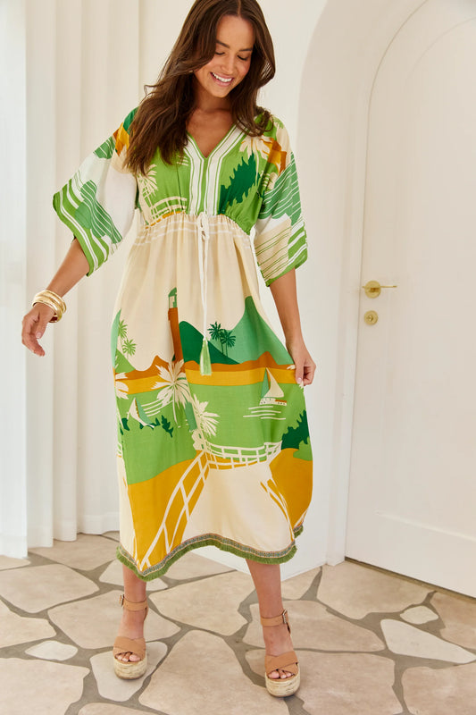 Woman wearing Solara Boheme Rio Dune Dress with green and warm earth tones, standing indoors with a relaxed smile