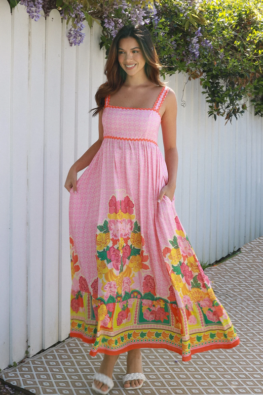 Woman wearing a boho pink floral dress standing against a white picket fence - Solara Boheme