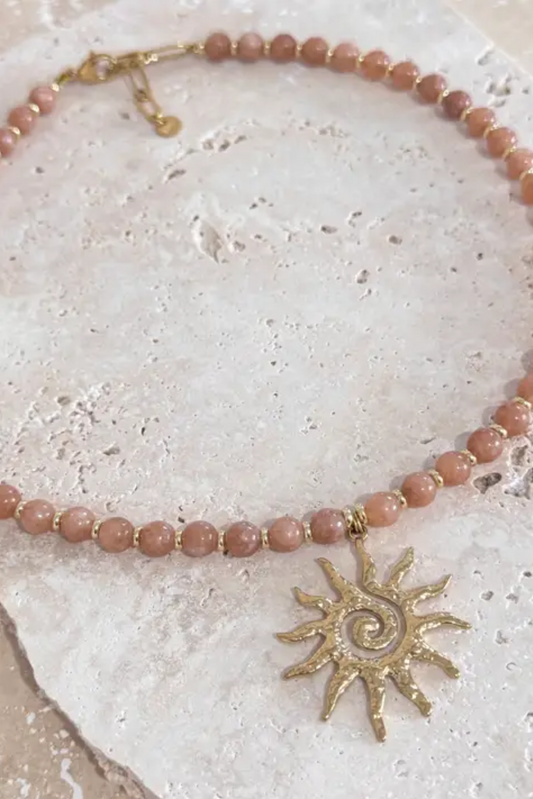Sunrise Stone Necklace by Solara Boheme features agate beads and a gold sun spiral charm on a natural stone background.