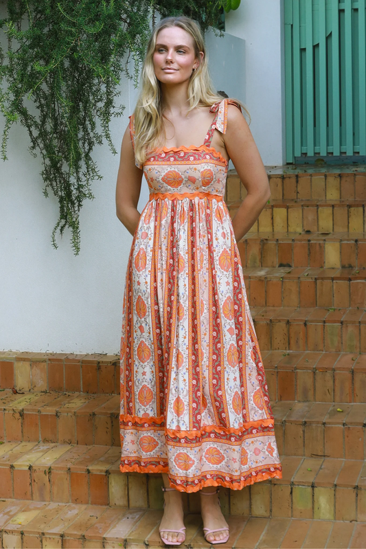 Woman wearing an orange and white patterned dress standing on steps with greenery in the background