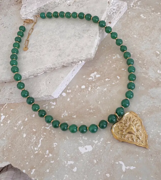 Green beaded necklace with a gold heart-shaped pendant on a stone surface