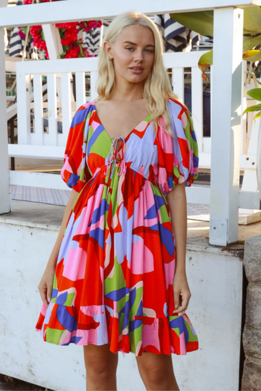 Woman wearing colorful Alberta Mini Dress with puff sleeves and ruffled hem standing outdoors near white fence