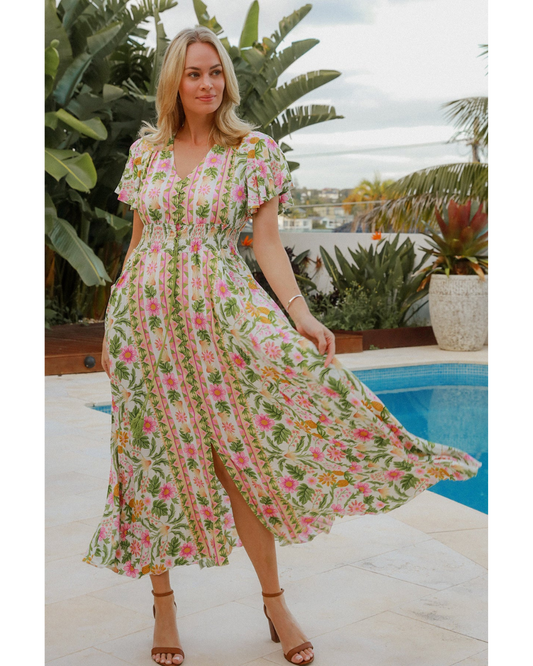 Woman wearing floral Alicia Maxi Dress by DreamCatcher standing by pool with tropical plants in background