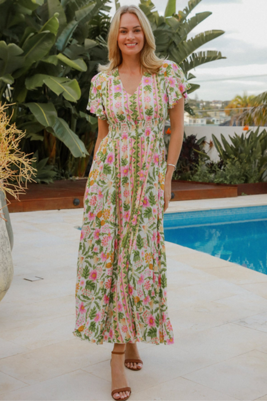 Woman wearing a floral Alicia Maxi Dress by DreamCatcher standing near a pool with tropical plants in the background.