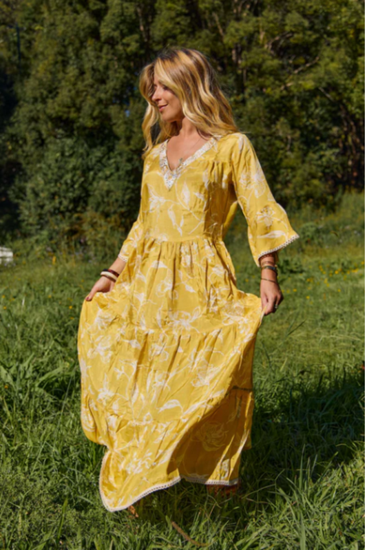 Woman wearing Solara Boheme Amber Maxi Dress in yellow with floral print and embroidered neckline outdoors in a green field
