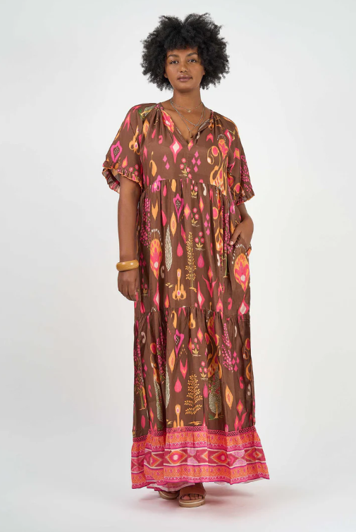 Woman wearing Solara Boheme Amisha Delta Maxi Dress with vibrant prints and contrasting border at hemline standing against white background