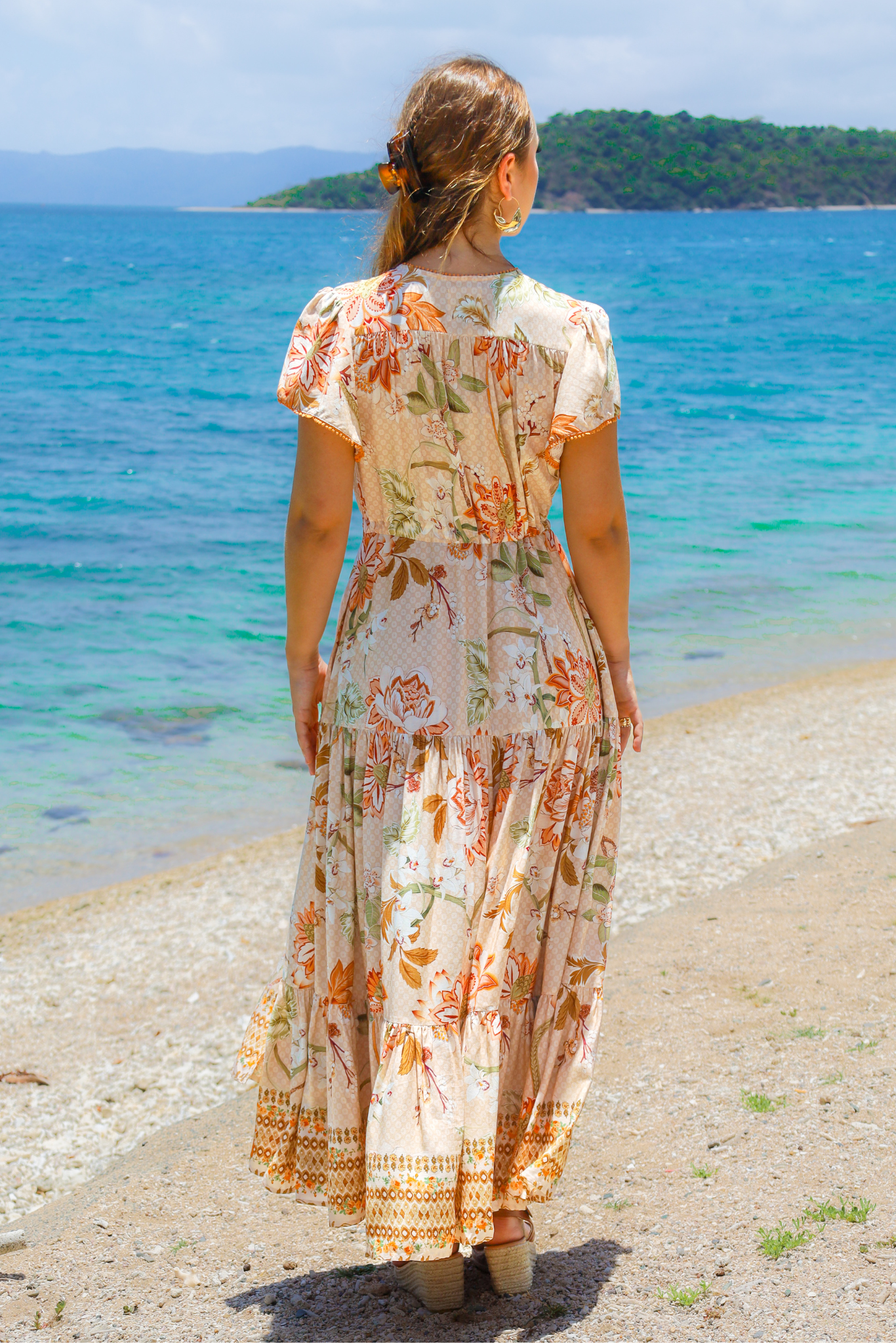 Woman in a floral dress standing on a beach with ocean and island in the background