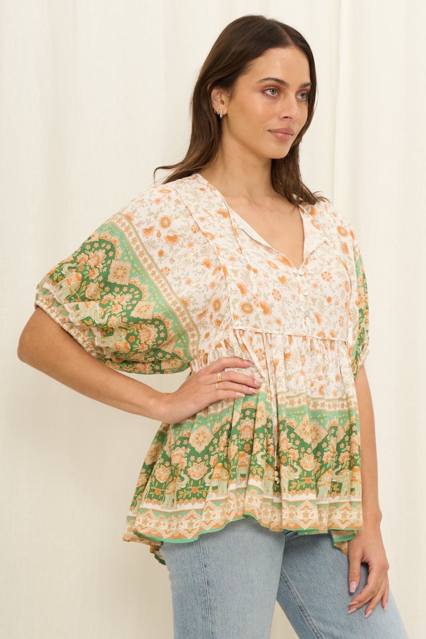 Woman wearing a floral blouse with green and orange patterns on a plain background