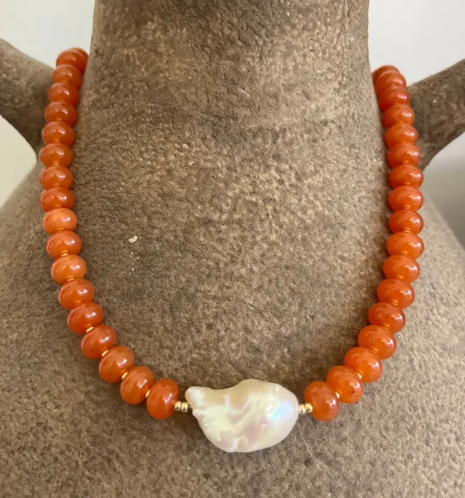Necklace with orange beads and a large white pearl on a brown mannequin bust.
