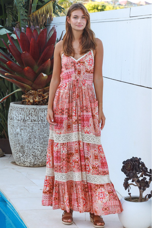 Woman wearing a red floral dress standing outdoors near a pool and plants.