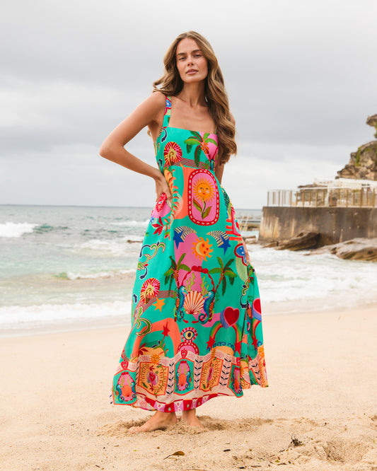 Woman in a colorful dress standing on a beach with ocean and sky in the background