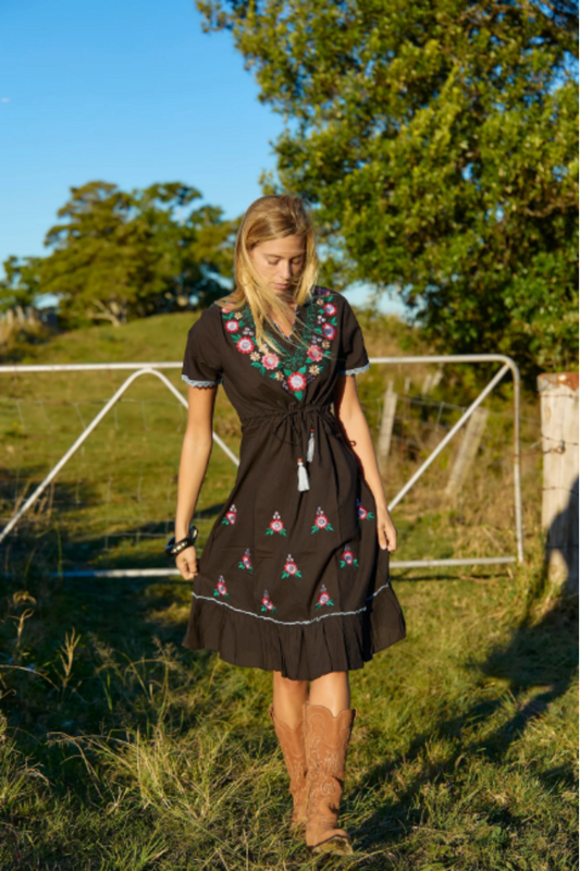 Woman wearing the Casey Mini Dress by Solara Boheme with floral embroidery standing outdoors on a sunny day