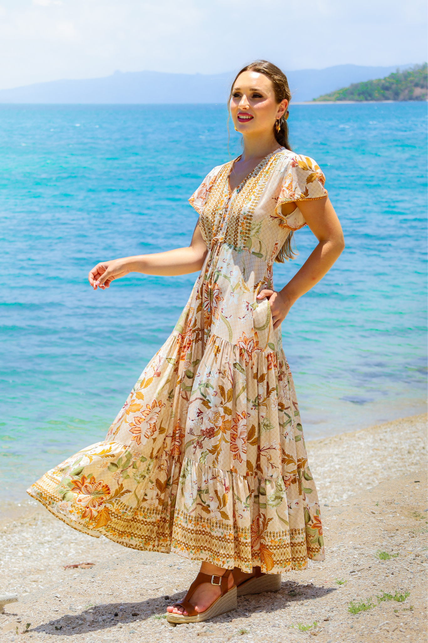 Woman in a floral dress standing on a beach with ocean in the background