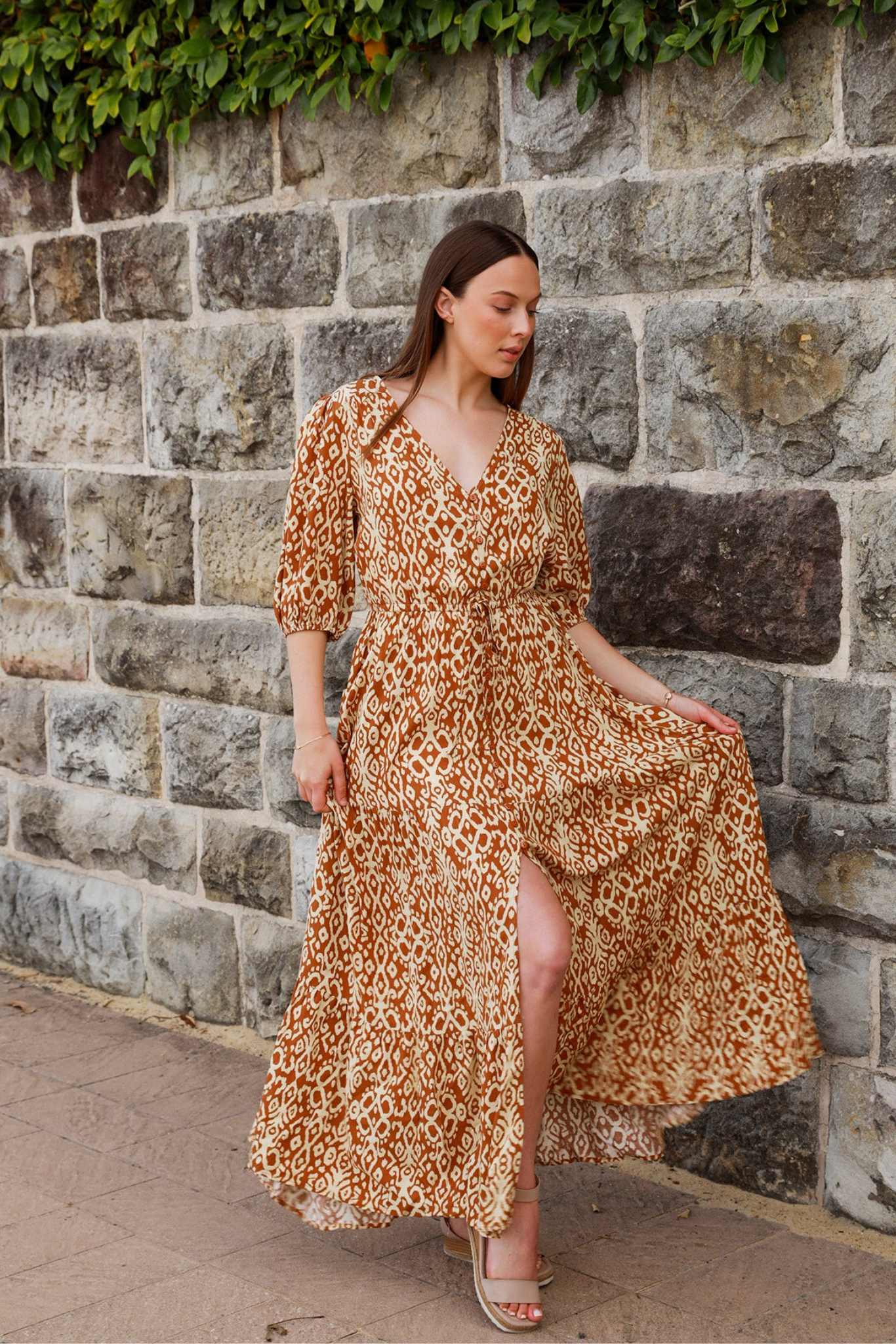 Woman wearing Solara Boheme Cora Maxi Dress with flowing orange patterned fabric against stone wall