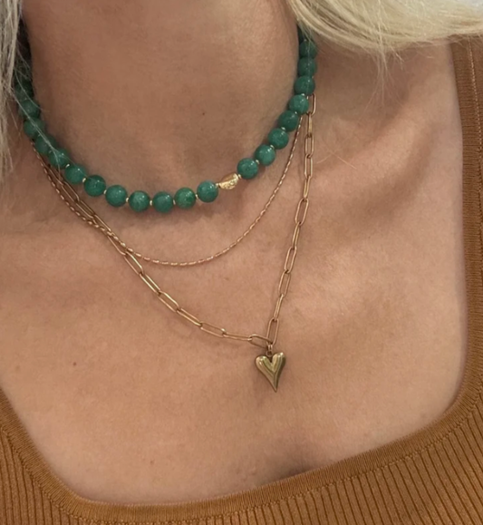 Close-up of a person wearing a green beaded necklace and a gold chain with a heart pendant.