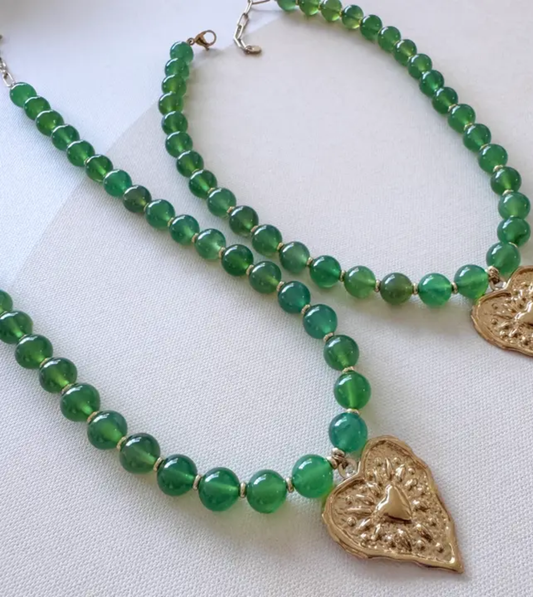 Green beaded necklace with gold heart pendants on a white background