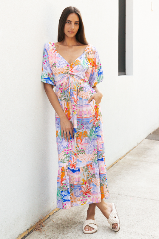 Woman wearing a colourful patterned dress standing against a white wall.