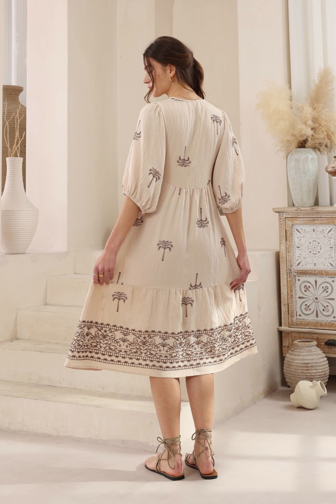 Woman wearing Desert Palm Midi Dress by Solara Boheme with embroidered palm trees and 3/4 sleeves in a neutral room setting