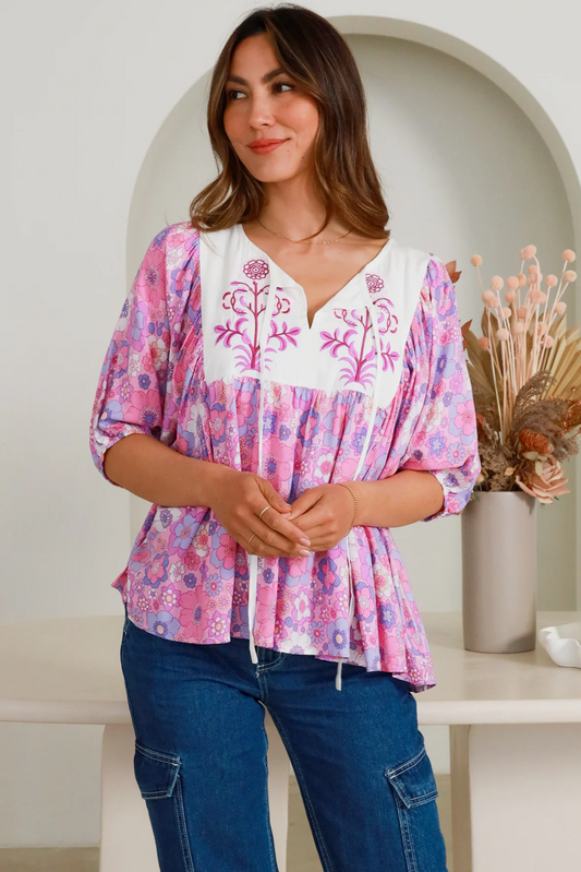 Woman wearing a pink and purple floral Eliana Blouse with white embroidered yoke and 3/4 sleeves paired with blue jeans