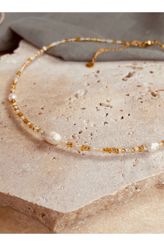 Delicate pebbly beach gold necklace with pearls, gold glass seed beads, and 24k gold plated Japanese beads on stone background
