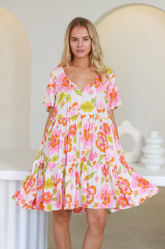 Woman wearing a bright floral Freya Mini Dress with pink, orange, and green patterns on a white background