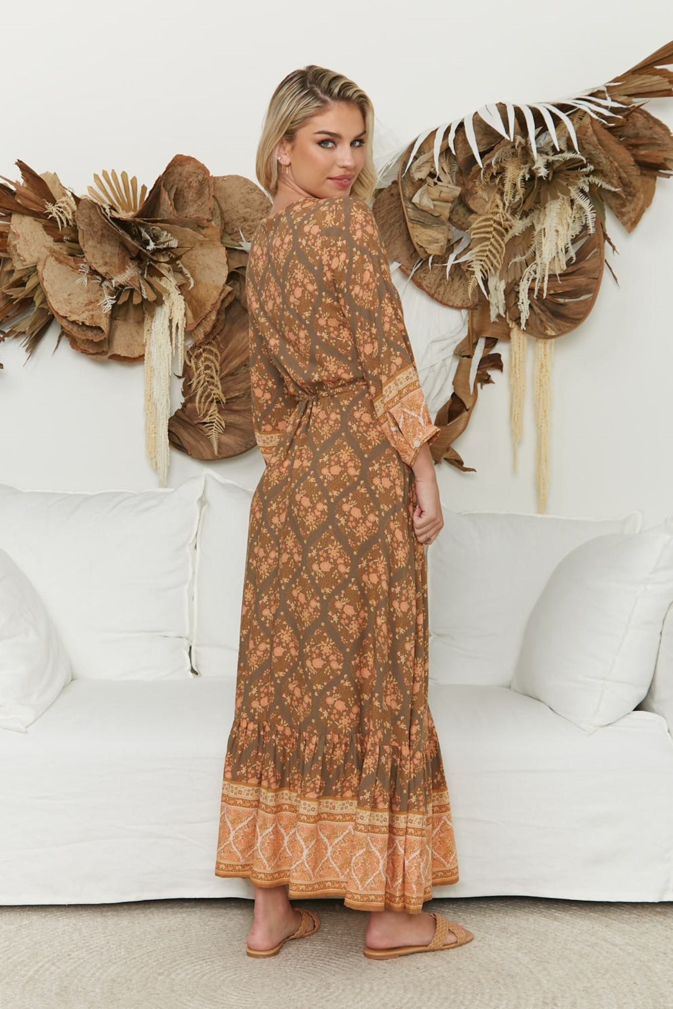 Woman in a patterned dress standing in a room with decorative elements.