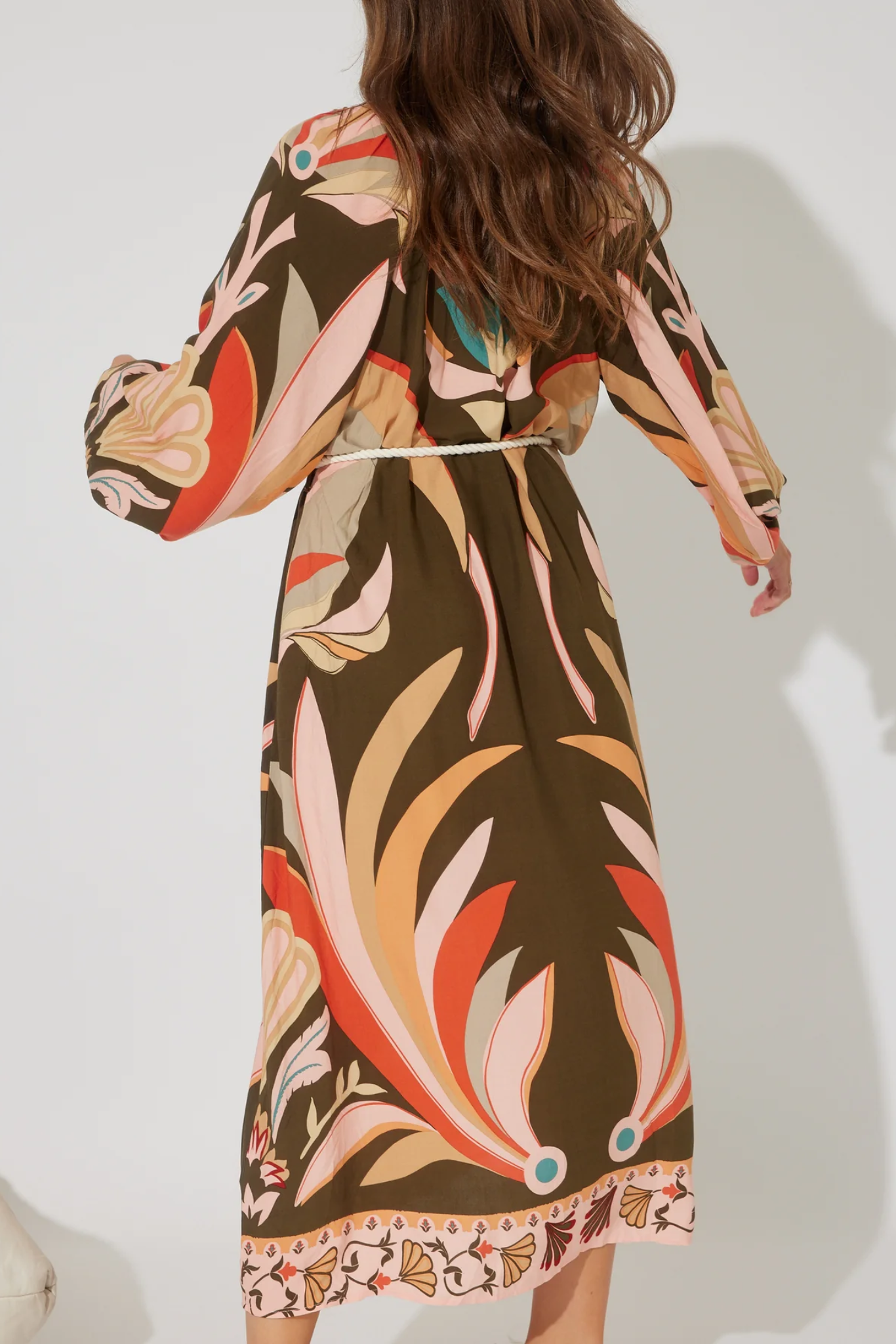 Back view of Koa Maxi Dress by Solara Boheme with vibrant floral pattern and rope tie belt on model with long hair