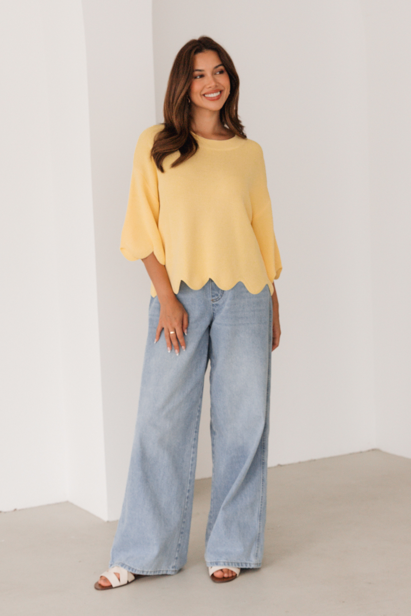 Woman wearing a yellow blouse and blue jeans against a white background