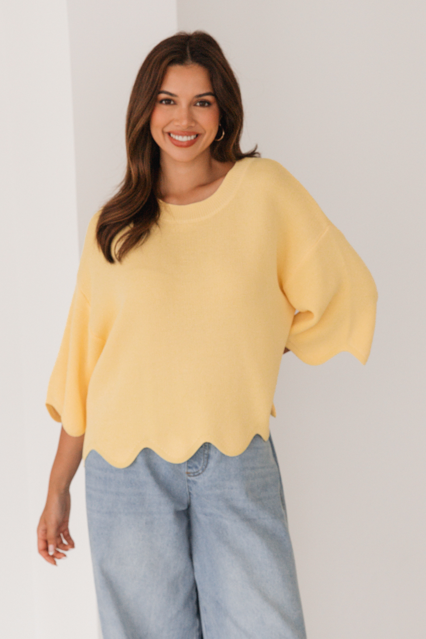 Woman wearing a yellow blouse and blue jeans against a plain background