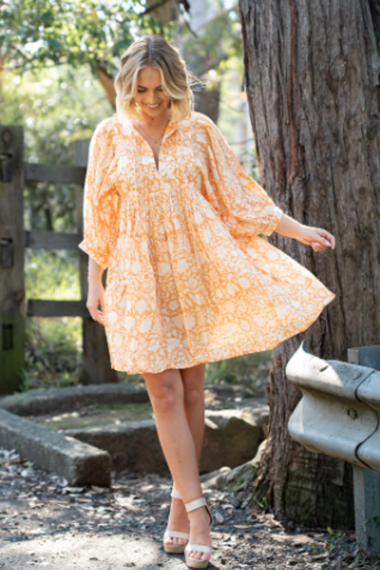 Woman wearing flowy Lisa Mini Dress by Solara Boheme in soft mandarin floral print outdoors by tree and fence