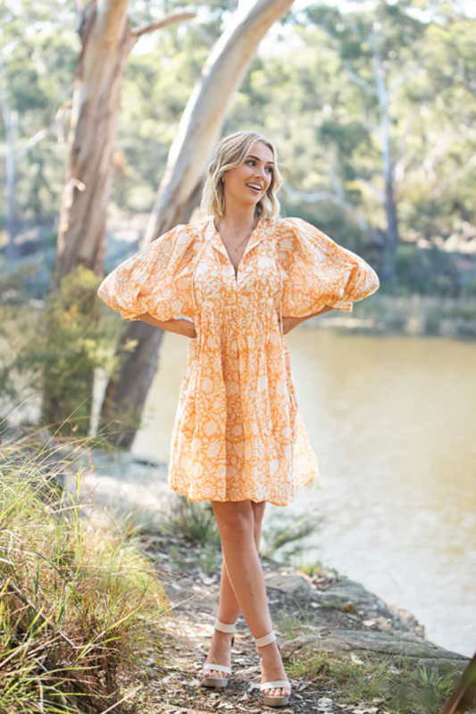 Woman wearing Solara Boheme Lisa Mini Dress with puff sleeves and floral print standing outdoors by water