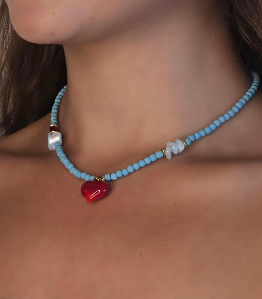 Necklace with blue beads and a red heart pendant on a person's neck.