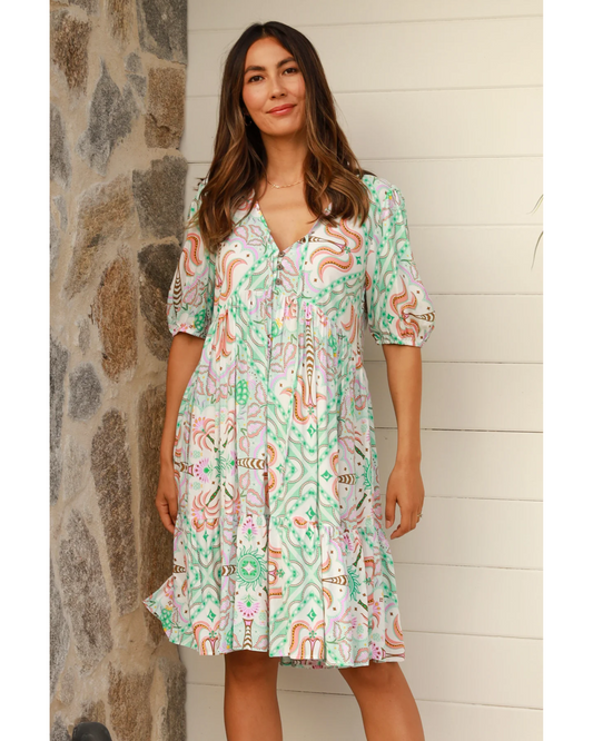 Woman wearing a patterned Luca Mini Dress from My Store standing by stone wall and white siding background
