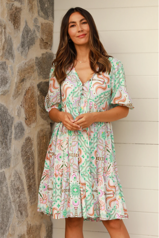 Woman wearing a Luca Mini Dress with colorful exclusive print by My Store standing against a stone wall and white door