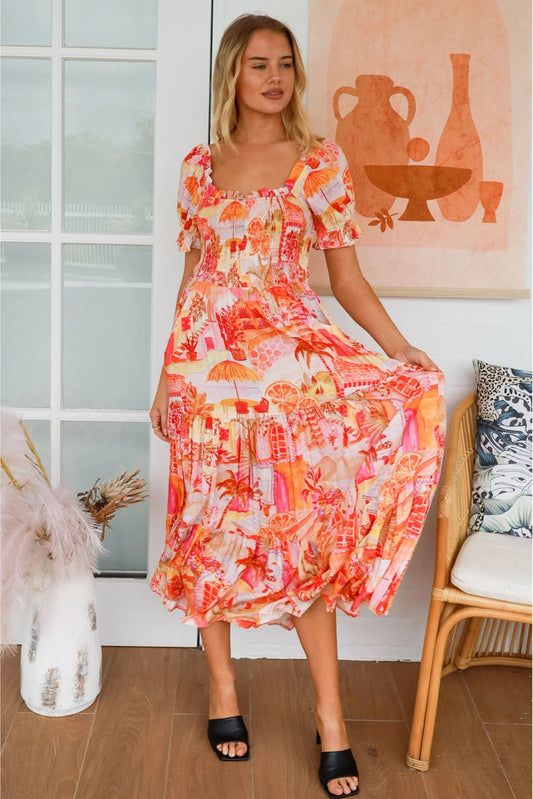 Woman wearing bright patterned Maribel Maxi Dress from My Store standing indoors by chair and window