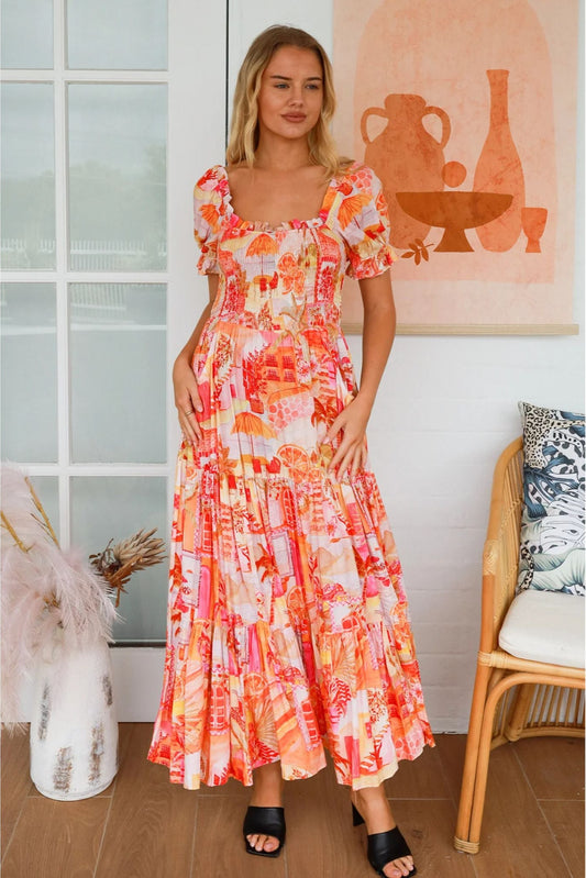 Woman wearing a vibrant Maribel Maxi Dress by My Store standing in a cozy, stylish room with natural light