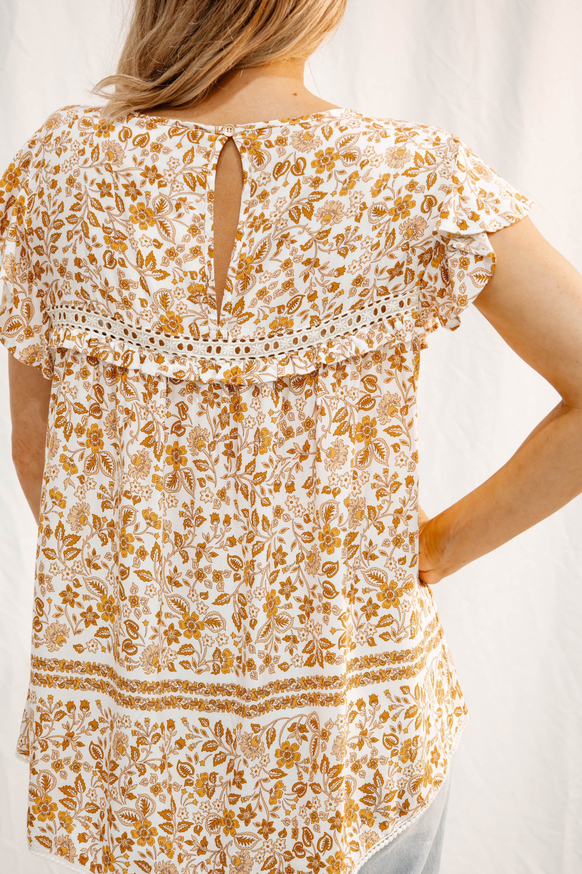 Back view of Meadow Flutter Blouse by Solara Boheme featuring warm honey floral print and lace trim detail