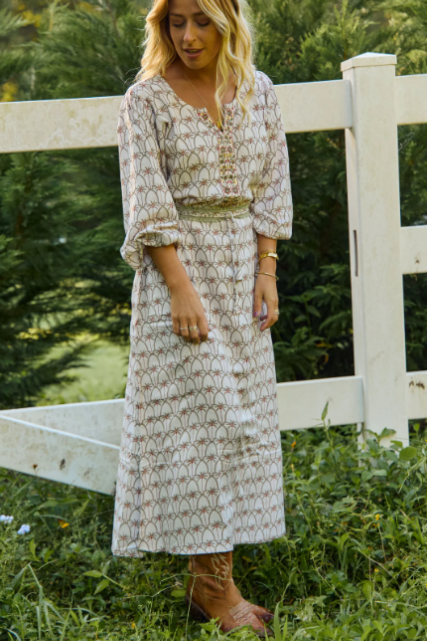 Woman wearing Palm Springs Maxi Dress by Solara Boheme standing near white fence in green outdoor setting