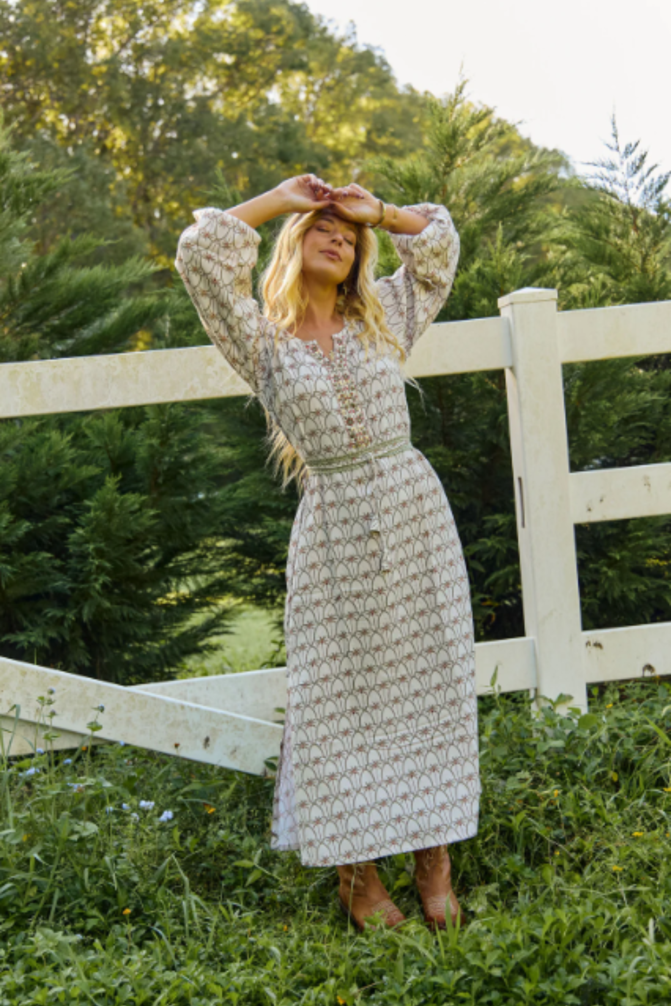 Woman wearing Solara Boheme Palm Springs Maxi Dress with nature-inspired print standing by white fence outdoors