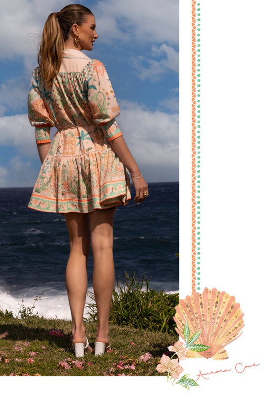 Woman wearing Palm Vista Mini Dress by Solara Boheme standing by ocean with blue sky and clouds in background