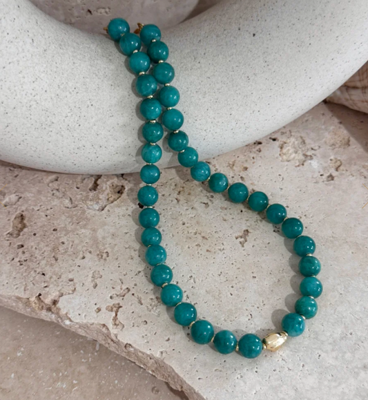 Turquoise beaded bracelet with a gold accent on a stone surface