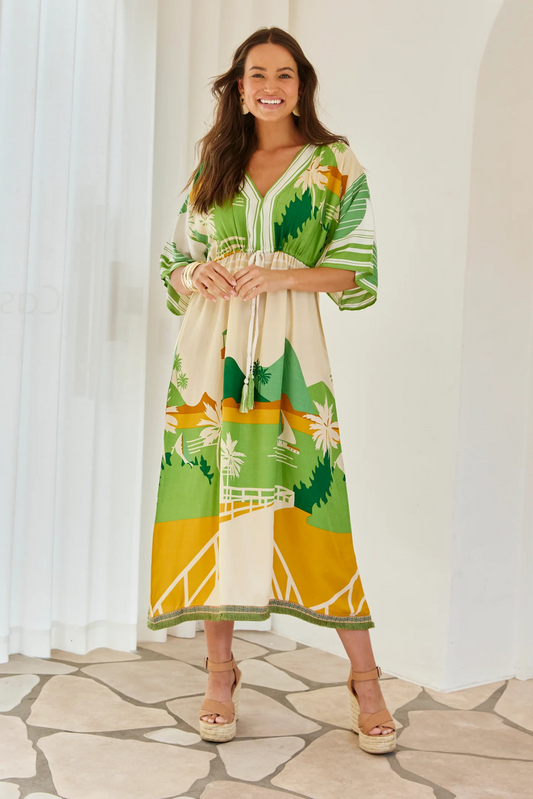 Woman wearing Solara Boheme Rio Dune Dress with lush green and warm tones, V-neckline, and fringed hem detail