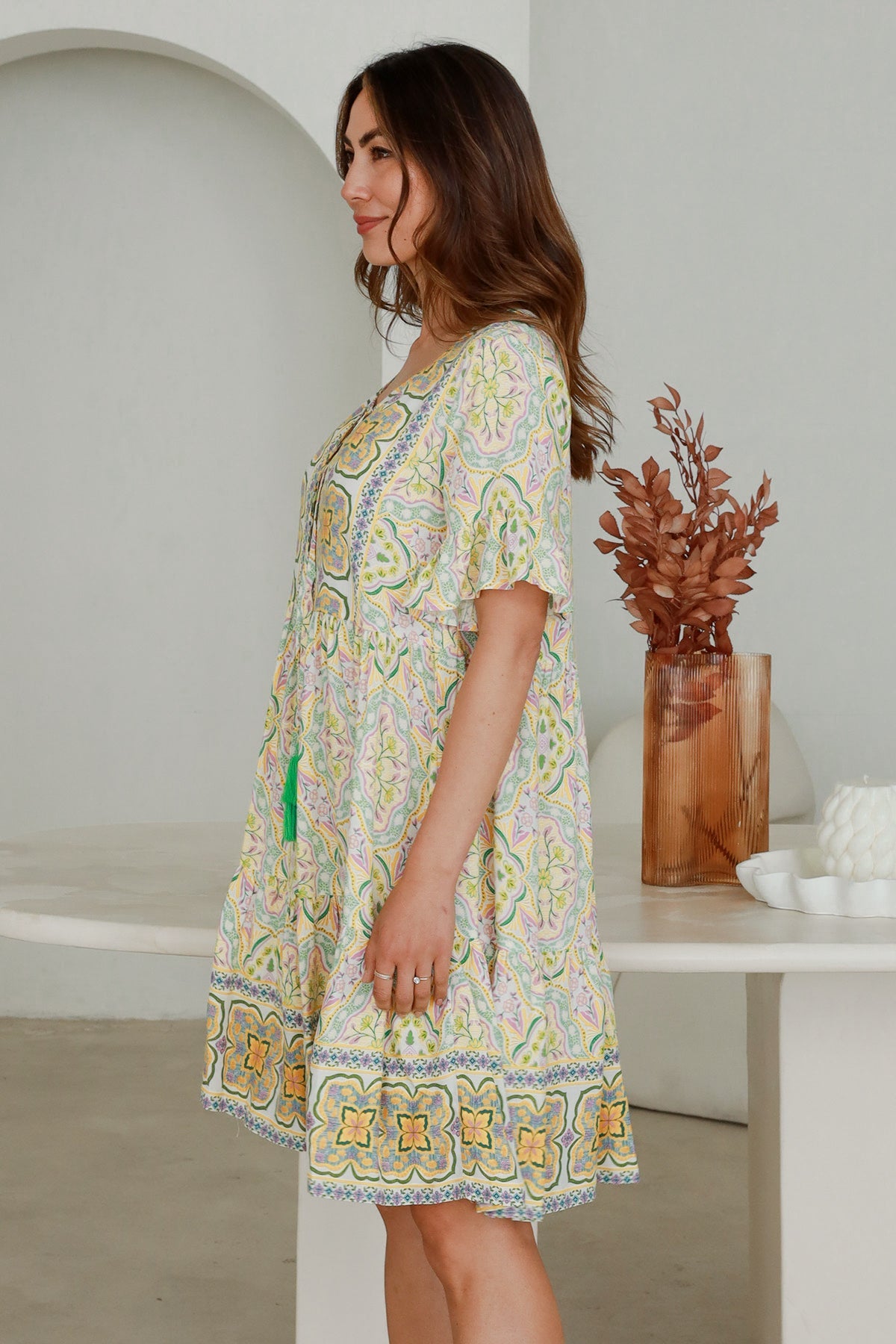 Woman wearing patterned Ryder Mini Dress from My Store standing indoors next to decorative vase with dried leaves