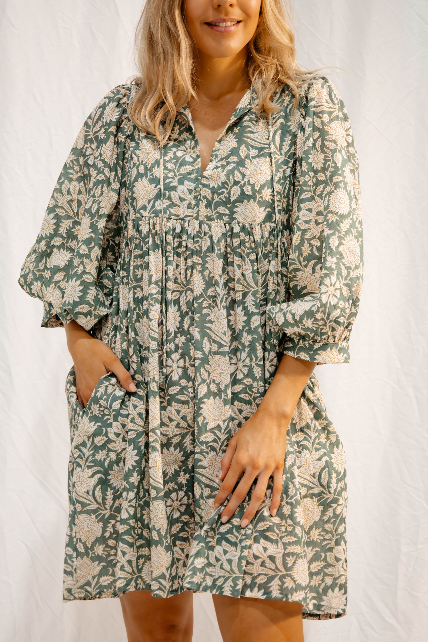 Woman wearing Solara Boheme's Sara Mini Dress in soft olive green with floral hand block print and pockets.