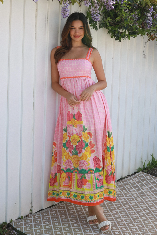 Woman wearing a boho pink floral dress standing against a white wall with greenery - Solara Boheme